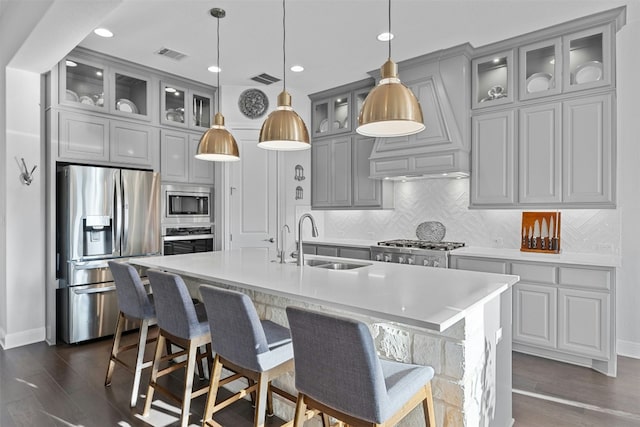 kitchen with sink, a kitchen island with sink, stainless steel appliances, decorative light fixtures, and decorative backsplash