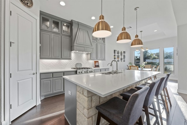 kitchen with sink, premium range hood, an island with sink, decorative light fixtures, and decorative backsplash