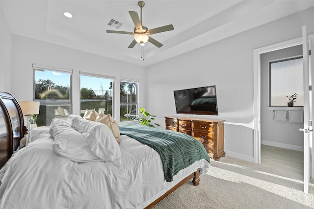 carpeted bedroom with ceiling fan and a tray ceiling