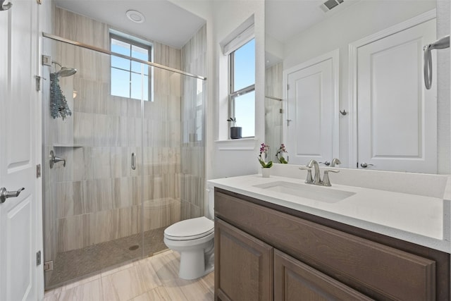 bathroom featuring vanity, toilet, a shower with shower door, and a healthy amount of sunlight