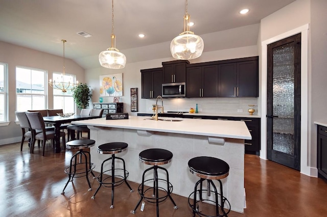 kitchen featuring backsplash, decorative light fixtures, sink, and an island with sink