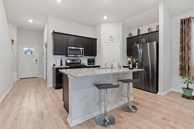 kitchen with a breakfast bar, stainless steel appliances, sink, light hardwood / wood-style flooring, and an island with sink