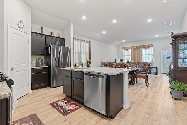 kitchen featuring lofted ceiling, stainless steel appliances, light hardwood / wood-style flooring, and a center island with sink