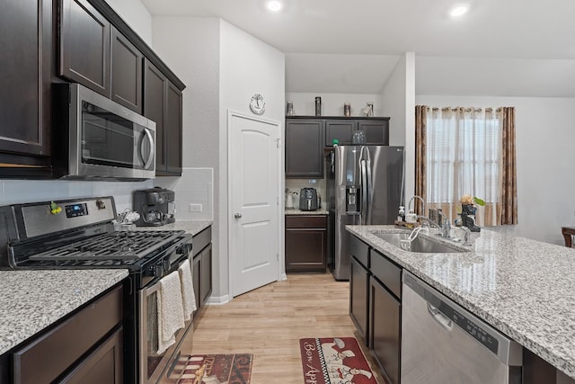 kitchen with light stone countertops, light wood-type flooring, backsplash, stainless steel appliances, and sink