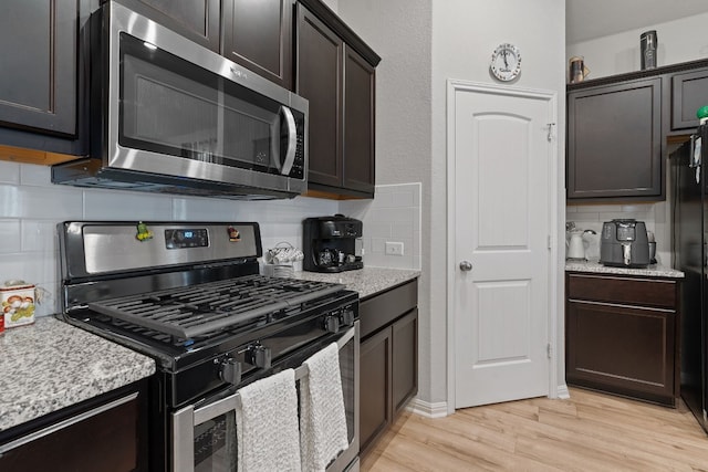 kitchen with dark brown cabinetry, decorative backsplash, light hardwood / wood-style flooring, and appliances with stainless steel finishes