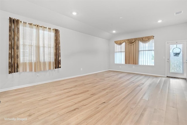 spare room featuring a healthy amount of sunlight, light wood-type flooring, and lofted ceiling