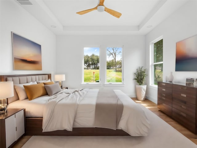 bedroom with a tray ceiling, ceiling fan, and light hardwood / wood-style floors