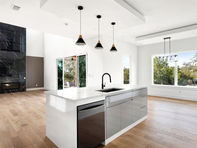 kitchen featuring light wood-type flooring, stainless steel dishwasher, sink, pendant lighting, and an island with sink