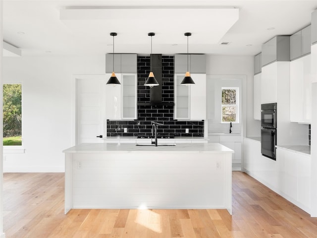 kitchen featuring sink, hanging light fixtures, tasteful backsplash, black double oven, and light hardwood / wood-style floors