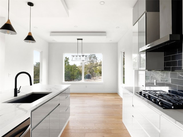 kitchen with decorative light fixtures, black gas stovetop, wall chimney exhaust hood, and sink