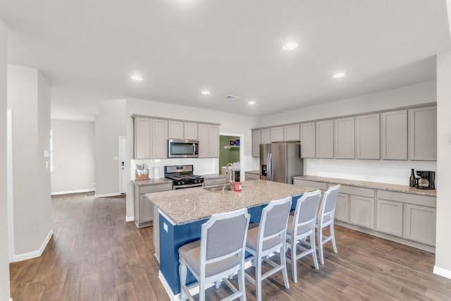 kitchen featuring light stone counters, stainless steel appliances, sink, a breakfast bar area, and an island with sink