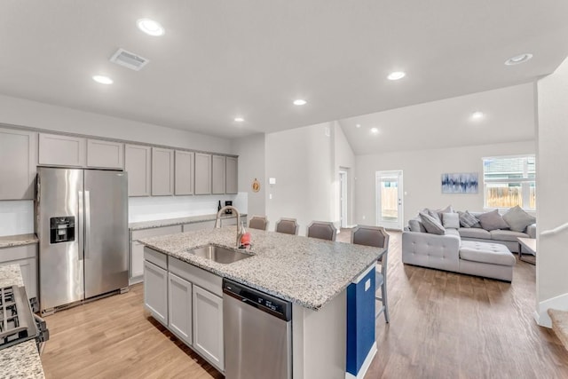 kitchen featuring appliances with stainless steel finishes, light stone counters, a breakfast bar, sink, and an island with sink