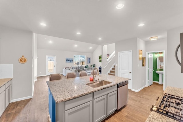 kitchen featuring sink, vaulted ceiling, a kitchen island with sink, appliances with stainless steel finishes, and light wood-type flooring