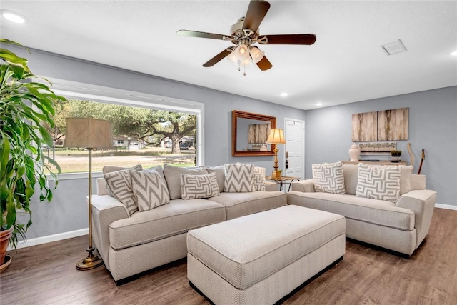 living room with a wealth of natural light, dark wood-type flooring, and ceiling fan