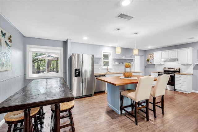 kitchen featuring wooden counters, stainless steel appliances, a kitchen island, white cabinetry, and hanging light fixtures