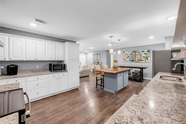 kitchen featuring wooden counters, sink, white cabinets, a kitchen island, and hanging light fixtures