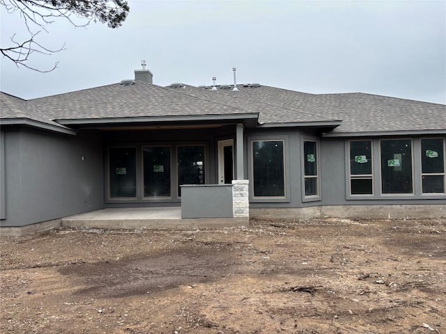 rear view of property featuring a patio area, a chimney, and a shingled roof