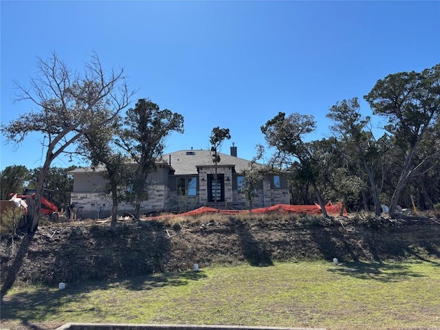 view of front of house with stone siding, a chimney, and a front lawn