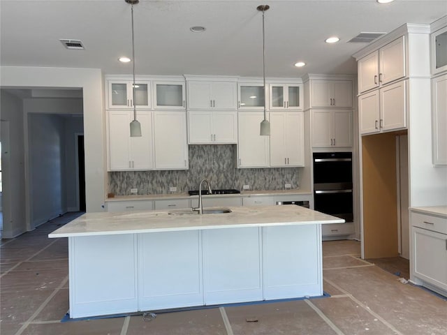 kitchen with glass insert cabinets, decorative light fixtures, and a center island with sink