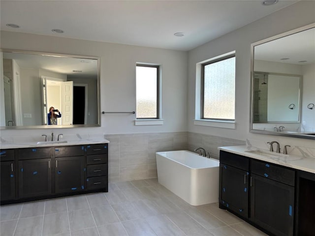 full bath with a sink, a freestanding bath, tile walls, and two vanities