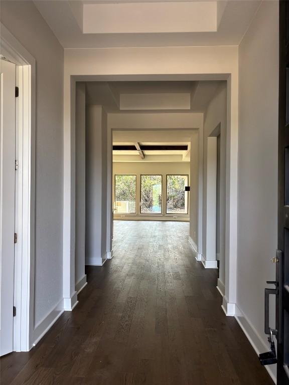 corridor with dark wood finished floors, a tray ceiling, and baseboards