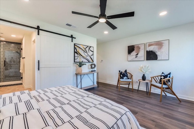 bedroom with a barn door, ceiling fan, and dark hardwood / wood-style flooring