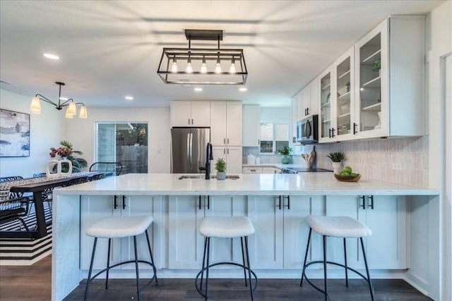 kitchen featuring kitchen peninsula, appliances with stainless steel finishes, tasteful backsplash, pendant lighting, and white cabinetry