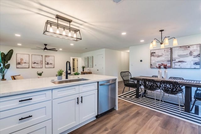 kitchen with pendant lighting, ceiling fan with notable chandelier, sink, stainless steel dishwasher, and white cabinetry