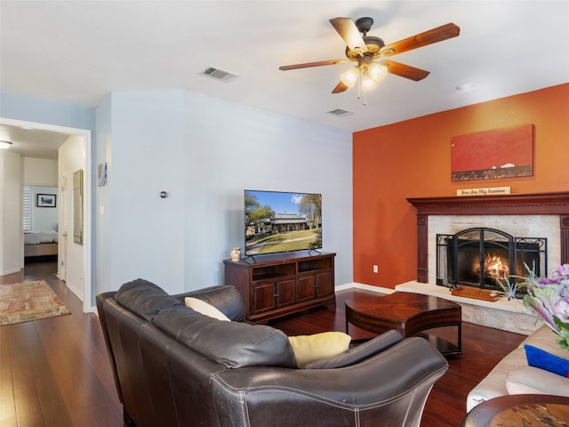 living room with a high end fireplace, ceiling fan, and dark wood-type flooring