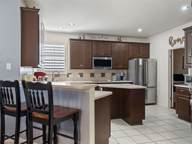 kitchen with a kitchen bar, dark brown cabinetry, stainless steel appliances, and a kitchen island