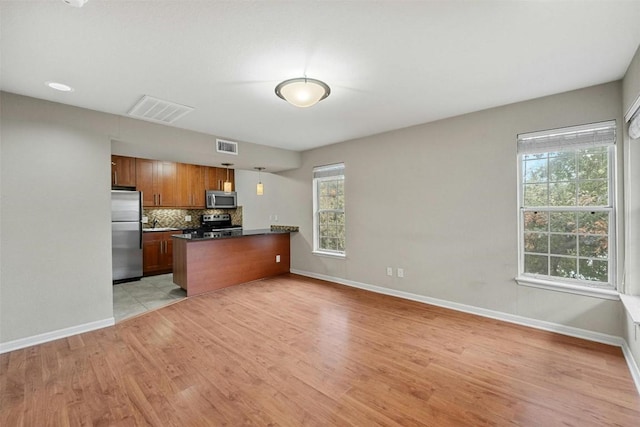 kitchen featuring backsplash, kitchen peninsula, stainless steel appliances, and light wood-type flooring