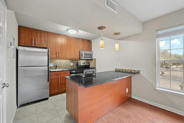 kitchen with stainless steel appliances, tasteful backsplash, kitchen peninsula, dark stone countertops, and pendant lighting