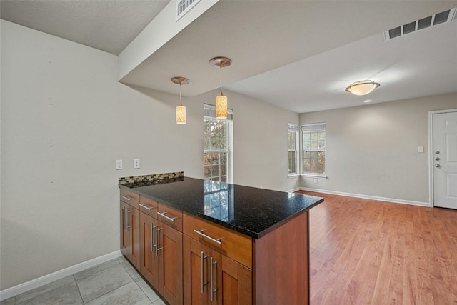 kitchen featuring kitchen peninsula, decorative light fixtures, and dark stone countertops