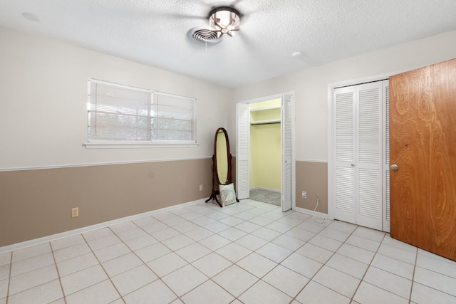 unfurnished bedroom featuring a textured ceiling, light tile patterned floors, and two closets