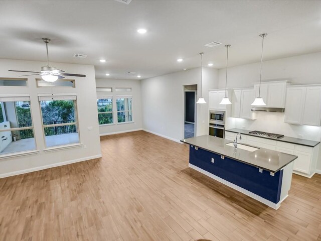 kitchen with stainless steel appliances, a kitchen island with sink, sink, white cabinetry, and hanging light fixtures