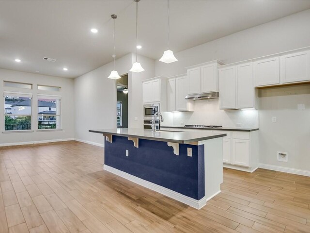 kitchen with light wood-type flooring, gas stovetop, white cabinets, hanging light fixtures, and a breakfast bar area