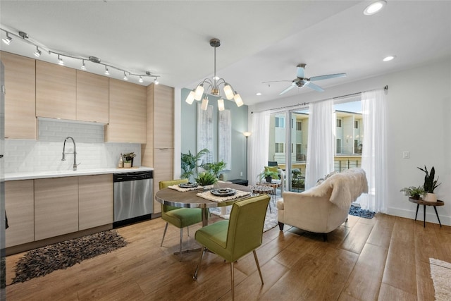 kitchen featuring tasteful backsplash, stainless steel dishwasher, ceiling fan with notable chandelier, pendant lighting, and light hardwood / wood-style floors