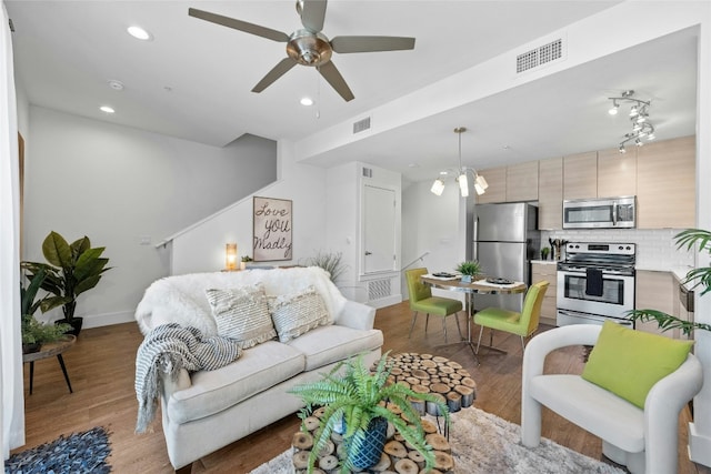 living room with ceiling fan with notable chandelier and light hardwood / wood-style flooring