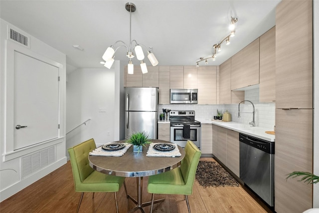 kitchen featuring light brown cabinets, sink, backsplash, decorative light fixtures, and appliances with stainless steel finishes