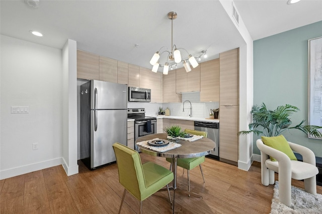 kitchen with tasteful backsplash, pendant lighting, stainless steel appliances, and light hardwood / wood-style flooring