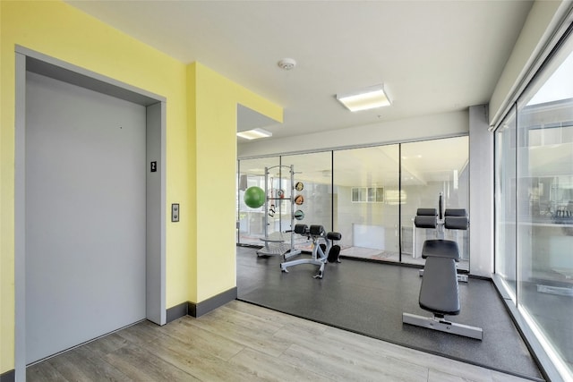 gym with elevator and light wood-type flooring