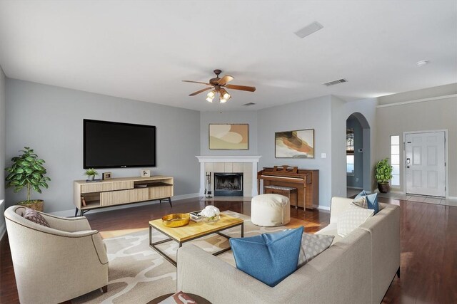 living room with dark hardwood / wood-style floors, ceiling fan, and a tiled fireplace