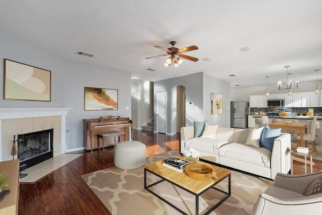 living room with a fireplace, light wood-type flooring, and ceiling fan with notable chandelier