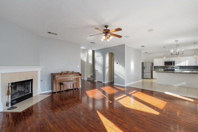 living room featuring ceiling fan with notable chandelier, a tile fireplace, and light hardwood / wood-style flooring