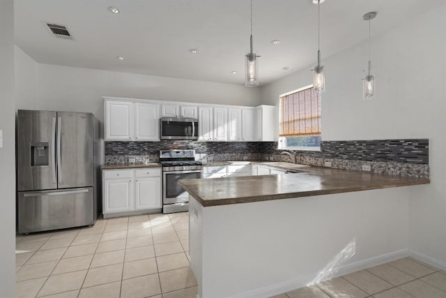 kitchen with white cabinets, light tile patterned floors, decorative light fixtures, kitchen peninsula, and stainless steel appliances