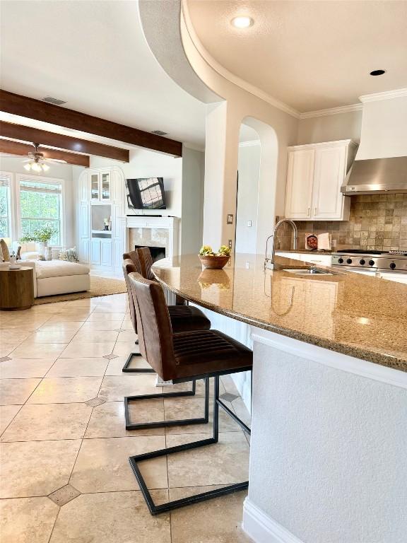 kitchen with a kitchen breakfast bar, sink, stone countertops, beam ceiling, and white cabinetry