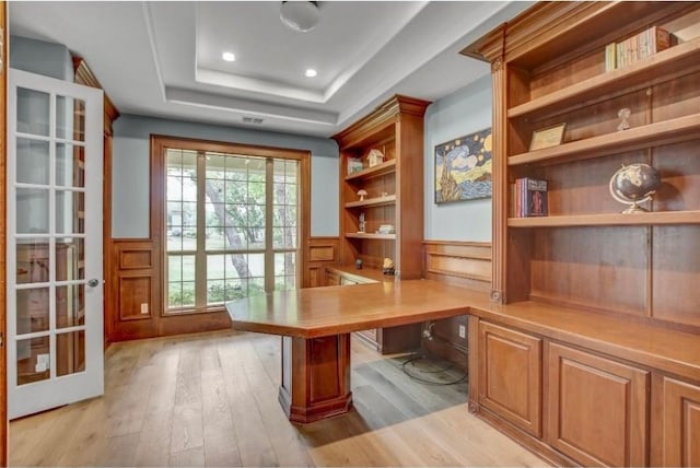 unfurnished office with a raised ceiling, built in features, light wood-type flooring, and built in desk