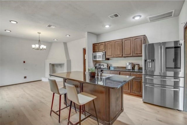 kitchen with stainless steel appliances, pendant lighting, a chandelier, a breakfast bar area, and a center island with sink