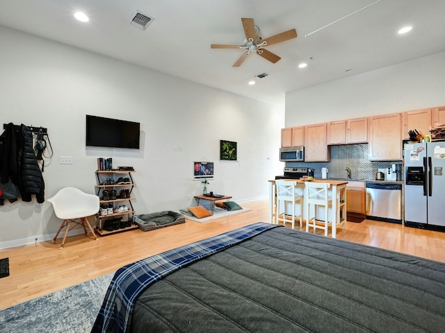 bedroom featuring ceiling fan, light hardwood / wood-style flooring, refrigerator with ice dispenser, and sink