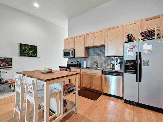 kitchen with appliances with stainless steel finishes, backsplash, sink, light brown cabinets, and light hardwood / wood-style floors